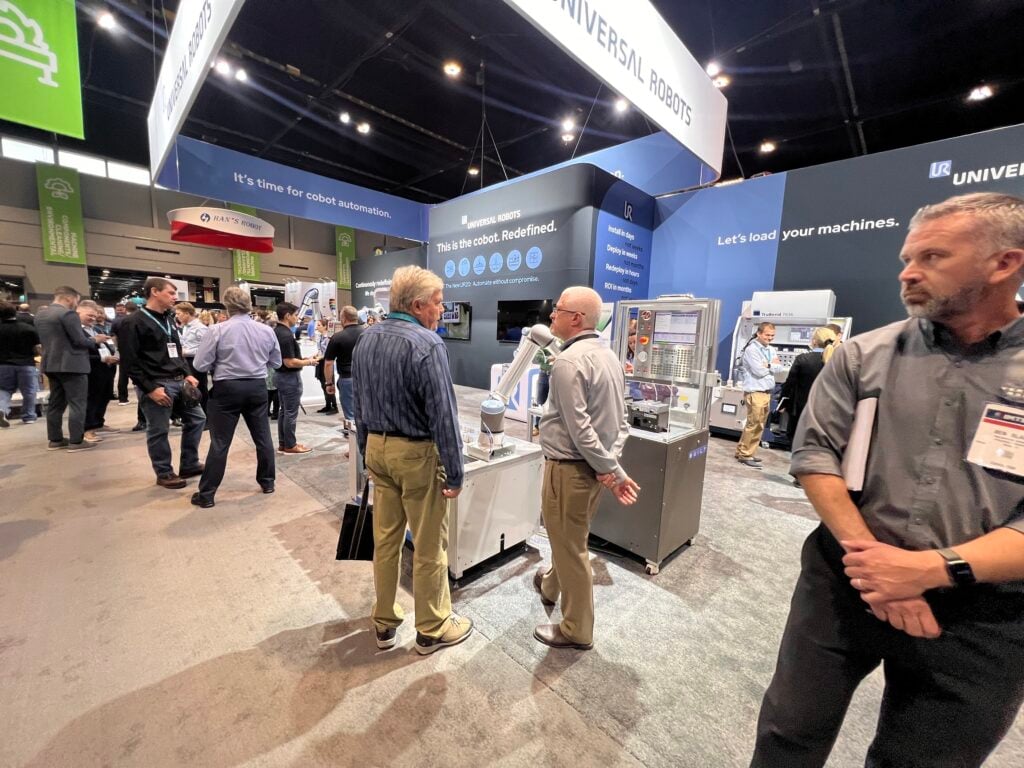 A busy exhibition floor displays people engaging with booths.