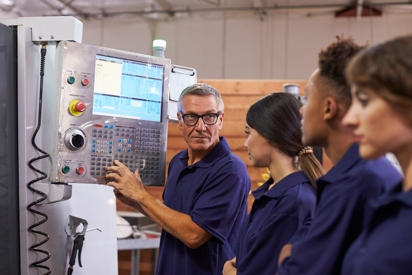 A teacher instructs students on a machine in a workshop setting.