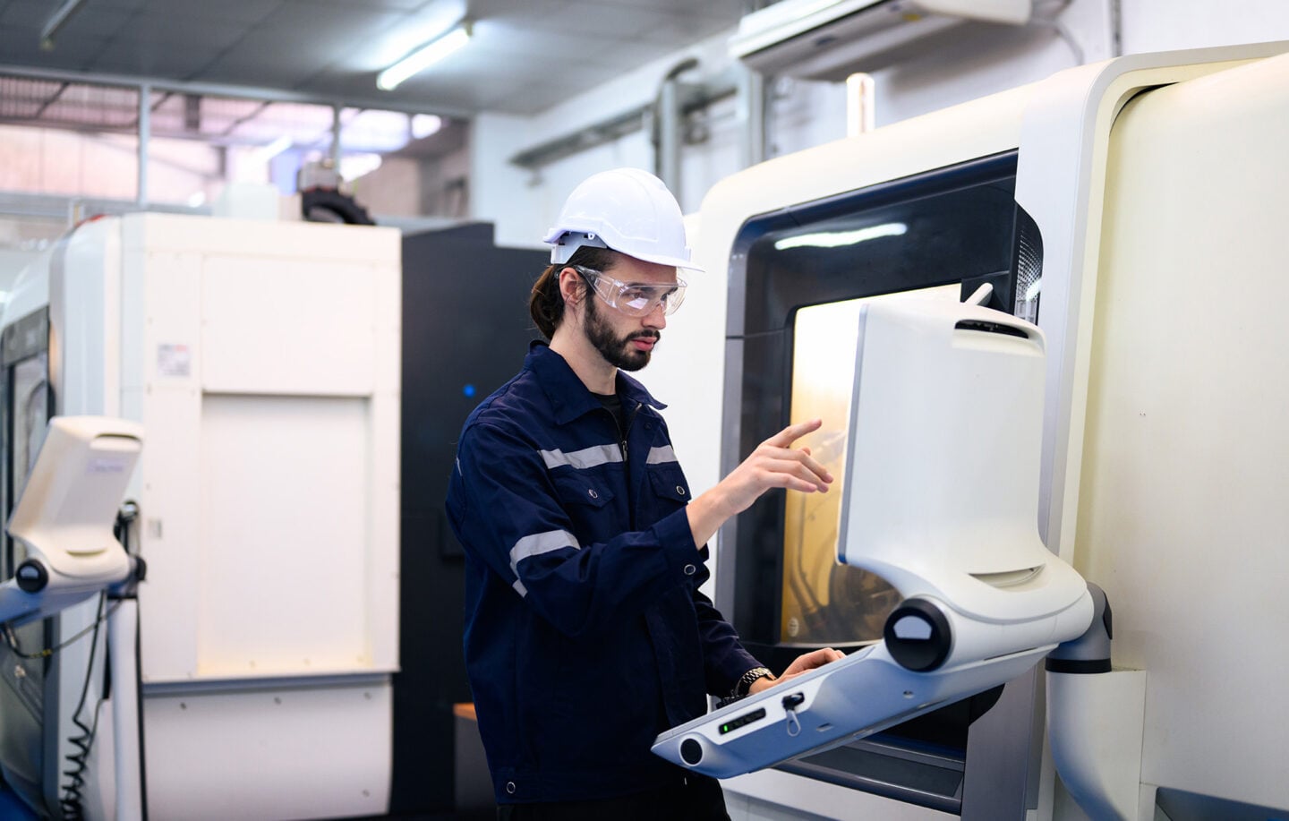 An engineer adjusts settings on a CNC machine in a workshop.