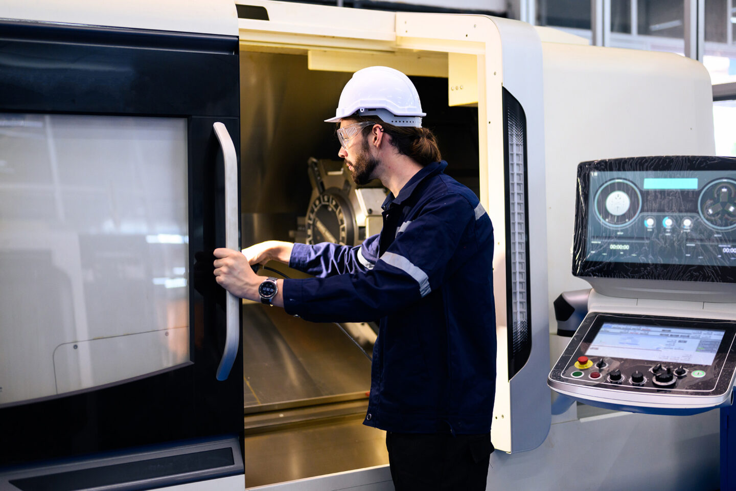 An engineer in a hard hat operates a machine in a workshop.