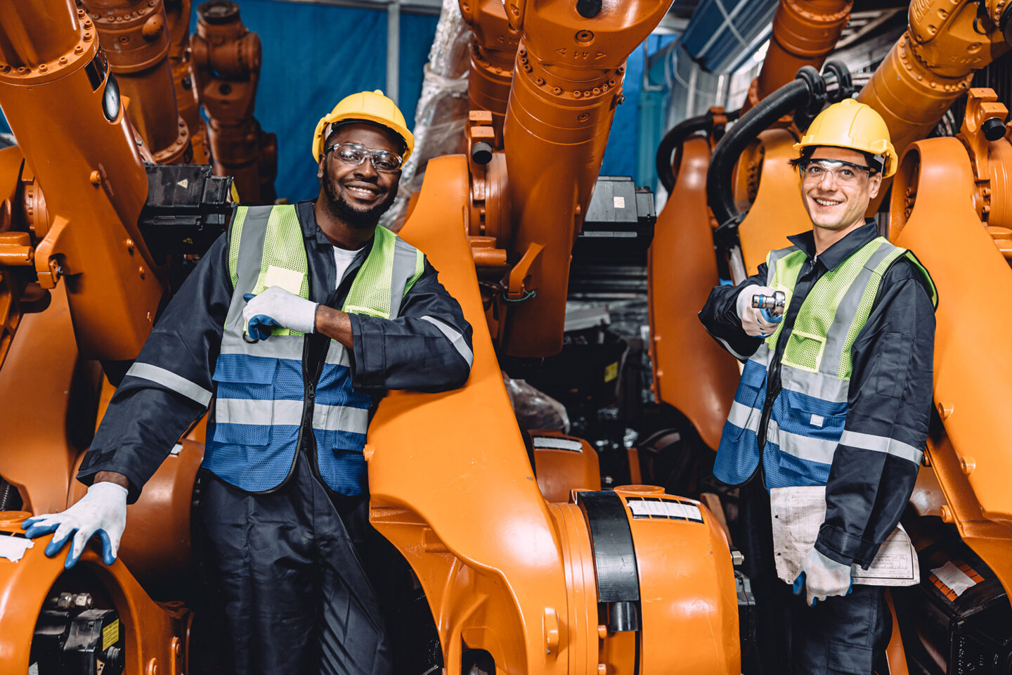 Two smiling workers pose confidently beside industrial robots.