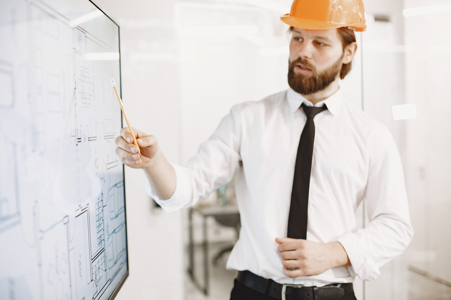 A young manager in a hard hat points at a screen displaying charts.