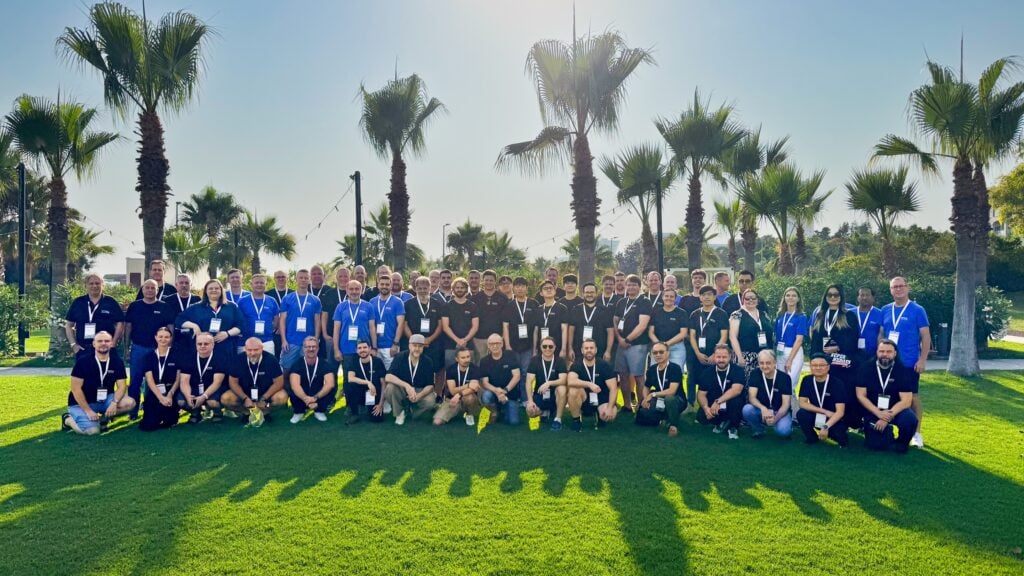 A large group of people poses together on a sunny day at a sports event.