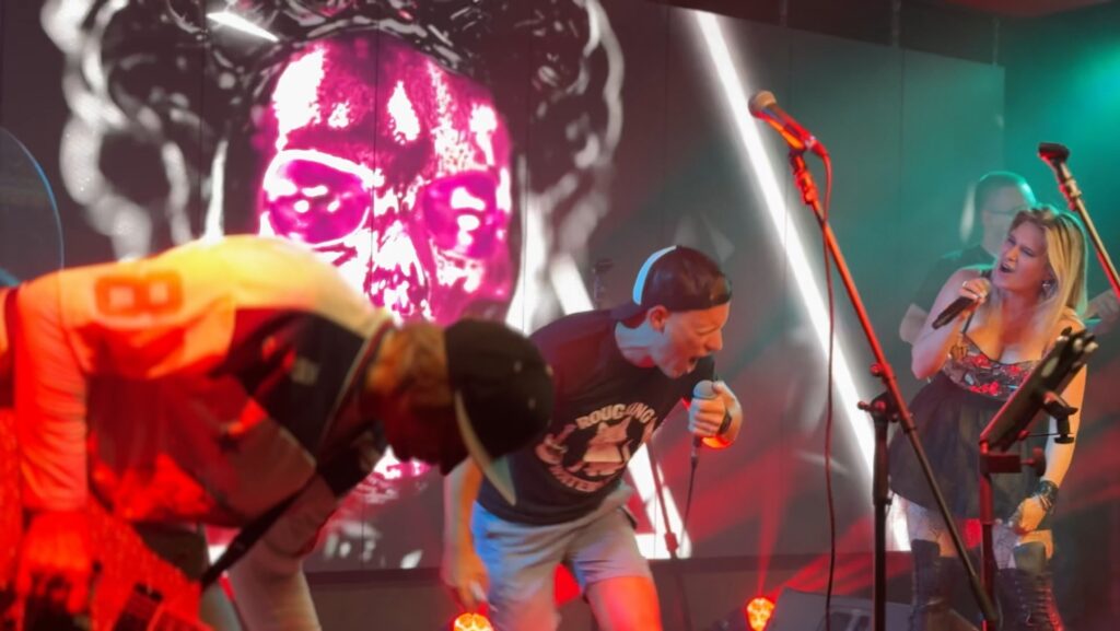 A performer sings energetically on stage with dynamic visuals behind.