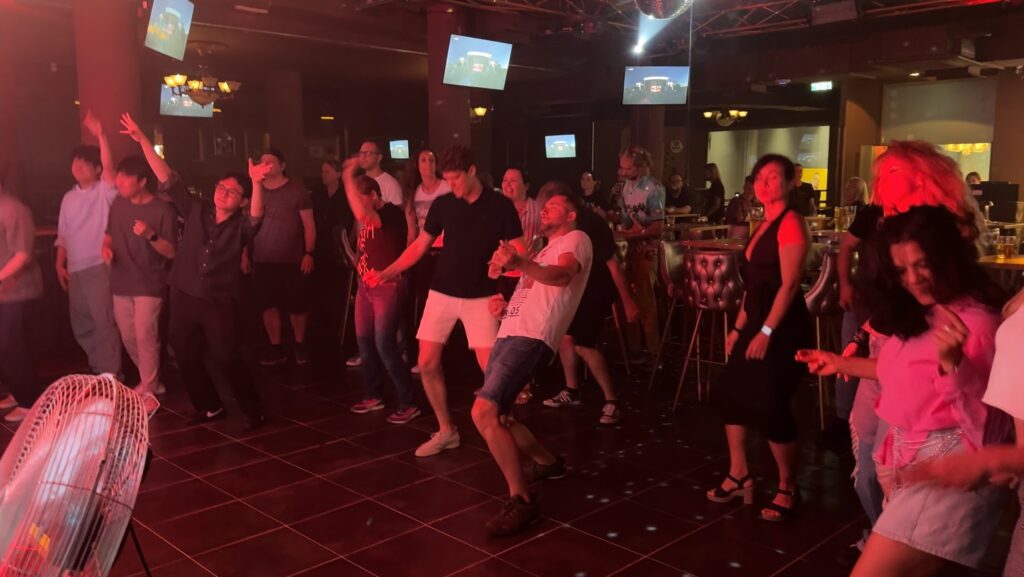A group of people dance energetically under colorful lights.