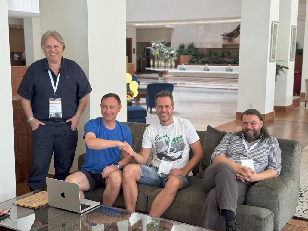 A group of four men are seated in a lounge, smiling and interacting.