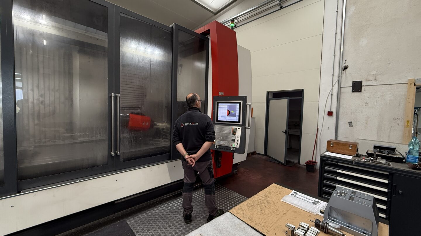 A technician observes a large CNC machine with a control panel.
