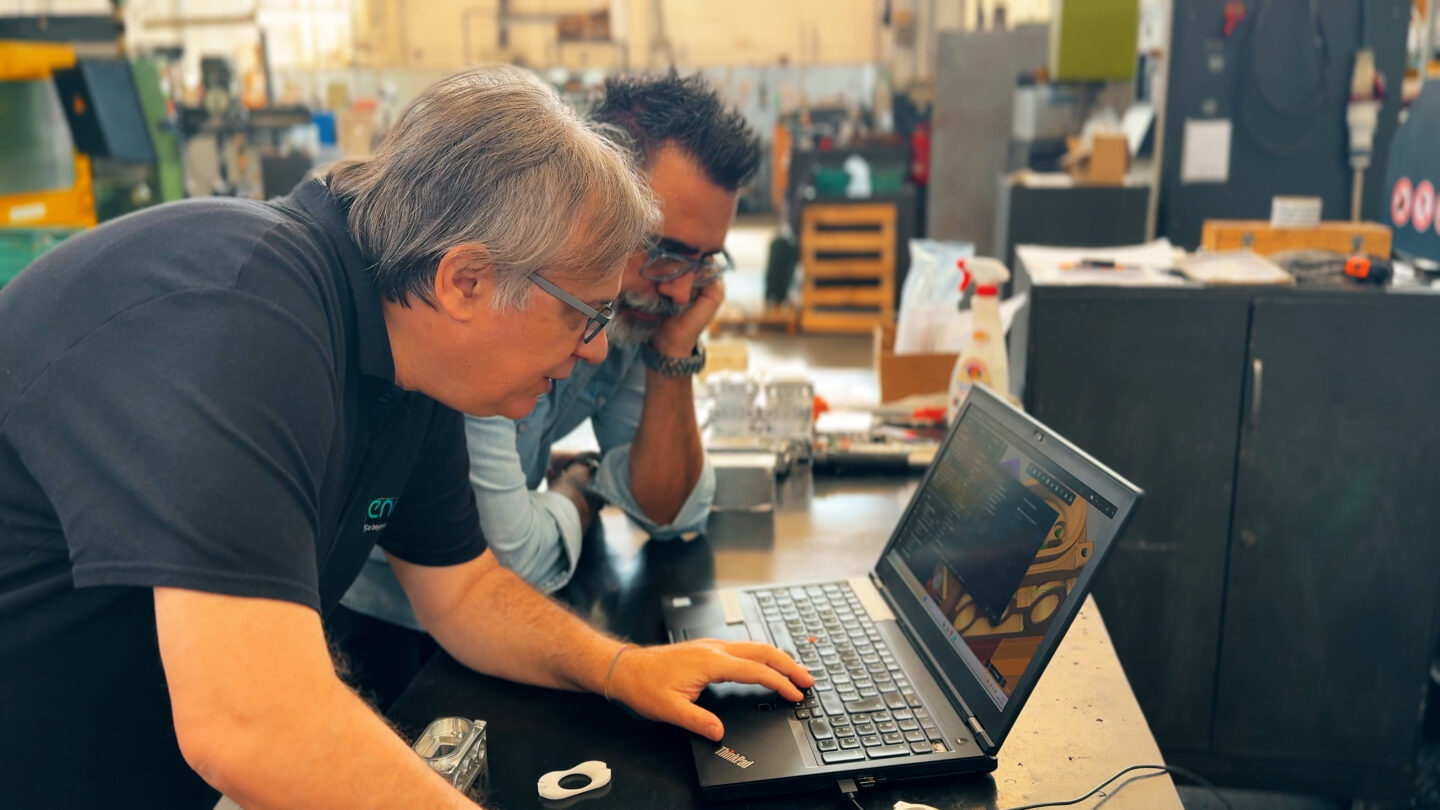 Two men collaborate while analyzing data on a laptop screen.