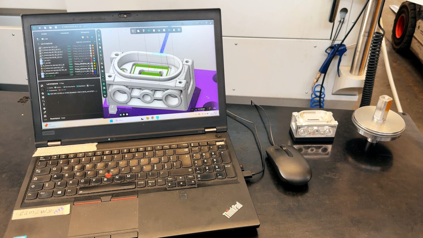 A laptop displays a 3D model of an engine part on its screen.