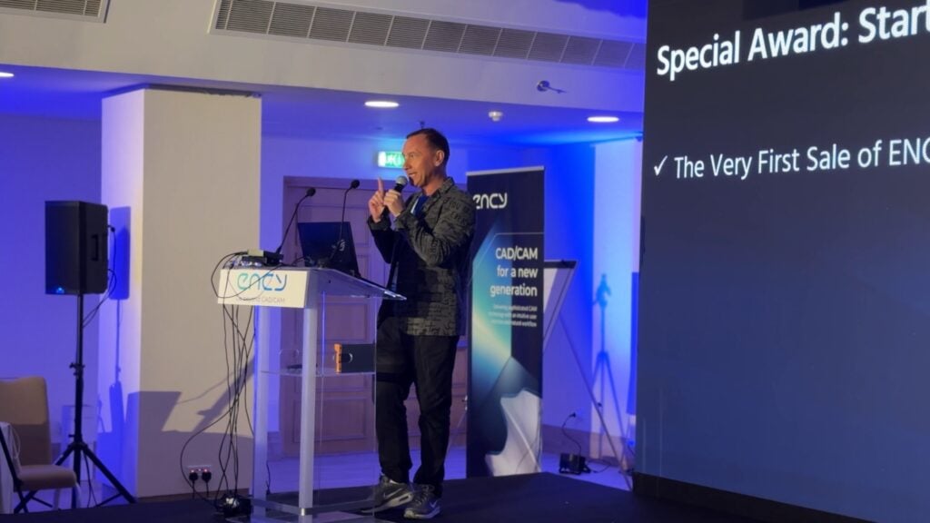 A speaker presents at a conference with visual aids displayed.