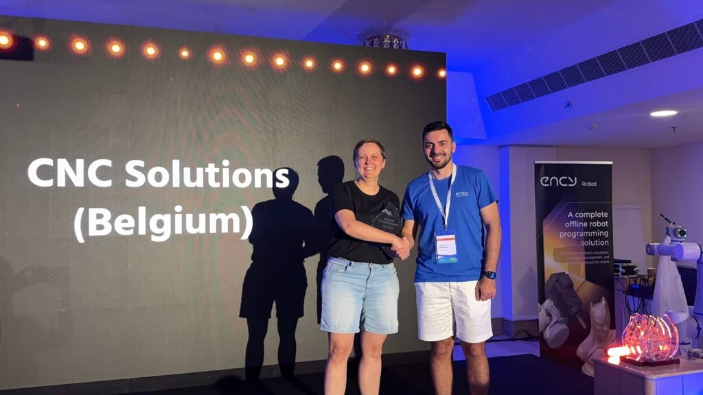 Two individuals shake hands on stage, smiling at a conference event.