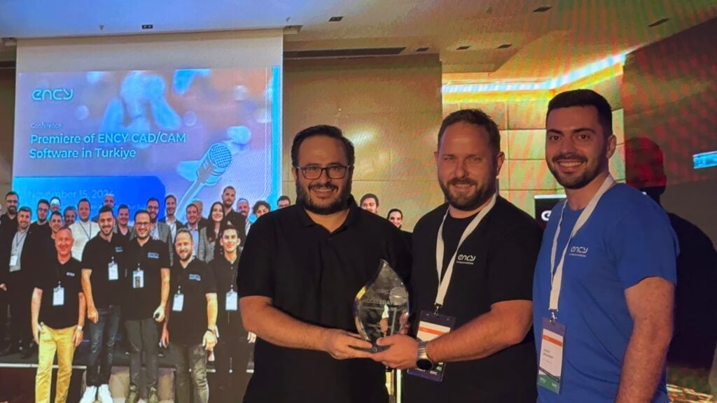 Three men stand together on stage, holding a trophy amid an audience.