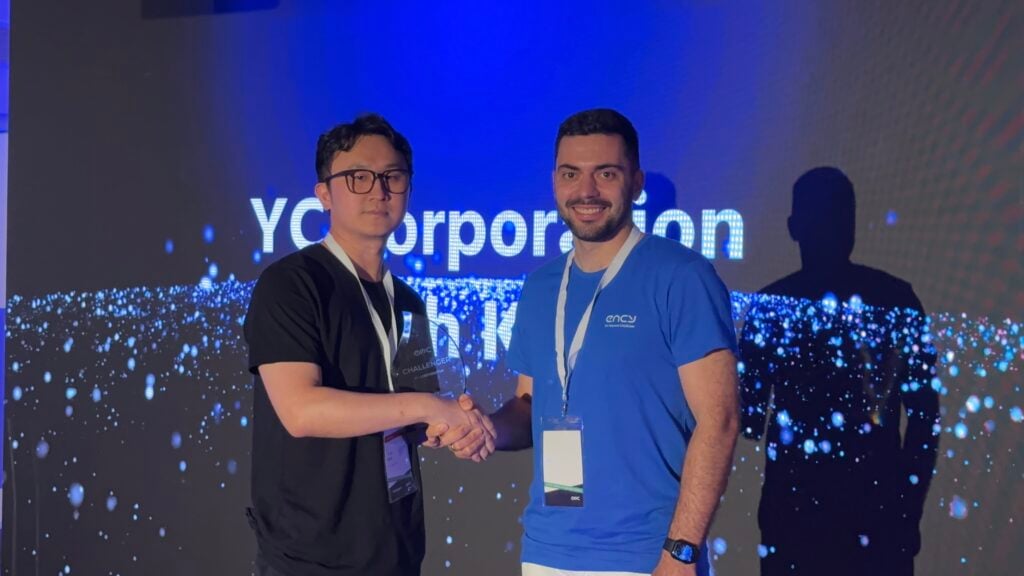 Two individuals shake hands on stage, smiling confidently.