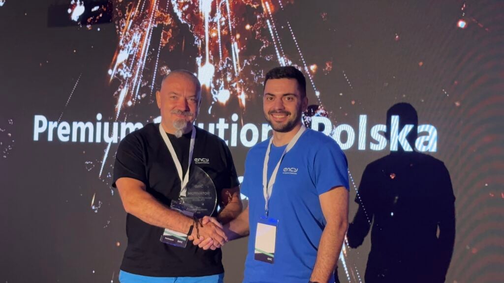 Two men shake hands on stage, celebrating an achievement together.