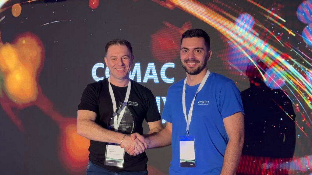 Two men shake hands on stage during a conference event.
