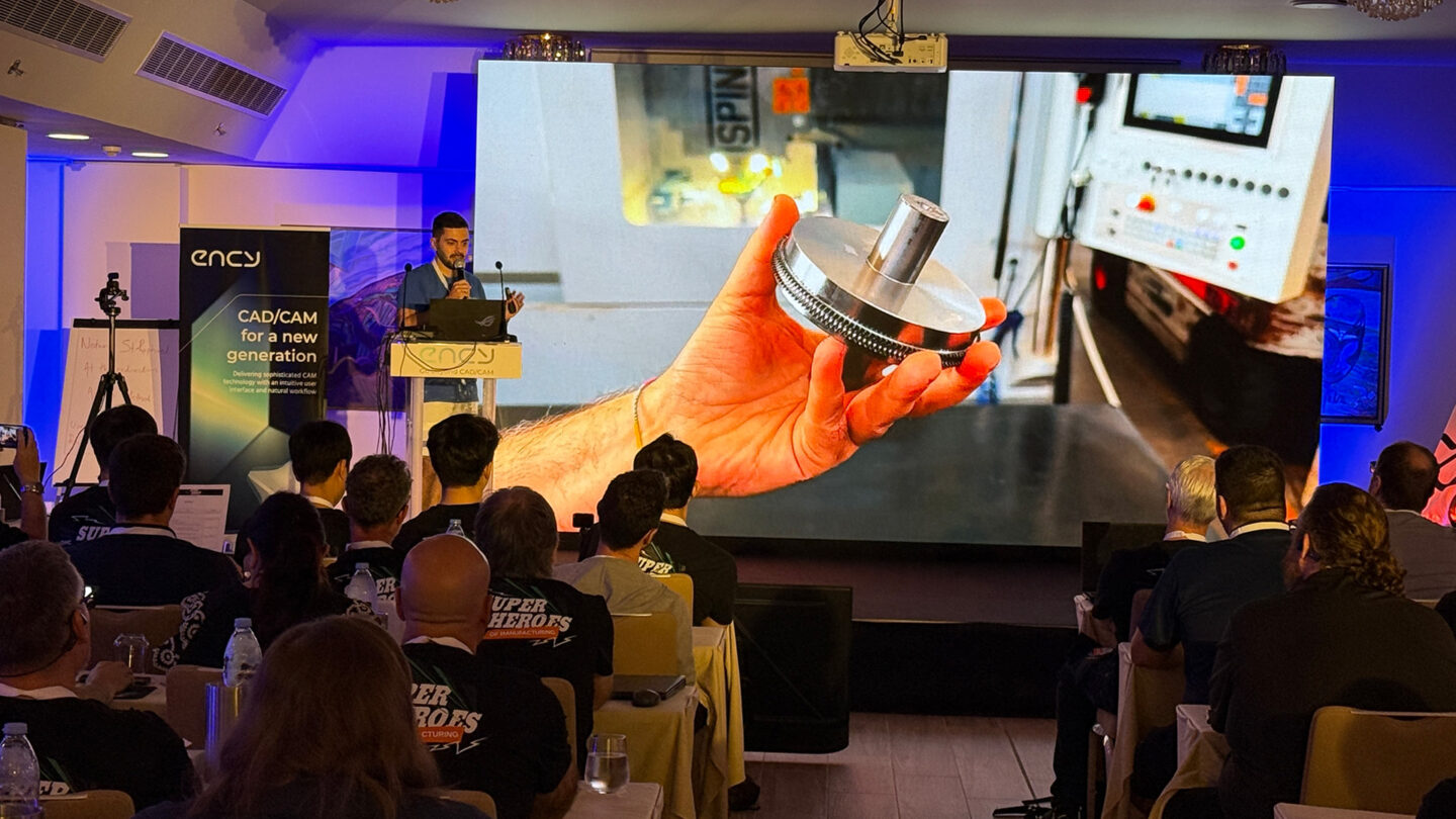 A speaker demonstrates a mechanical part during a presentation to an audience.