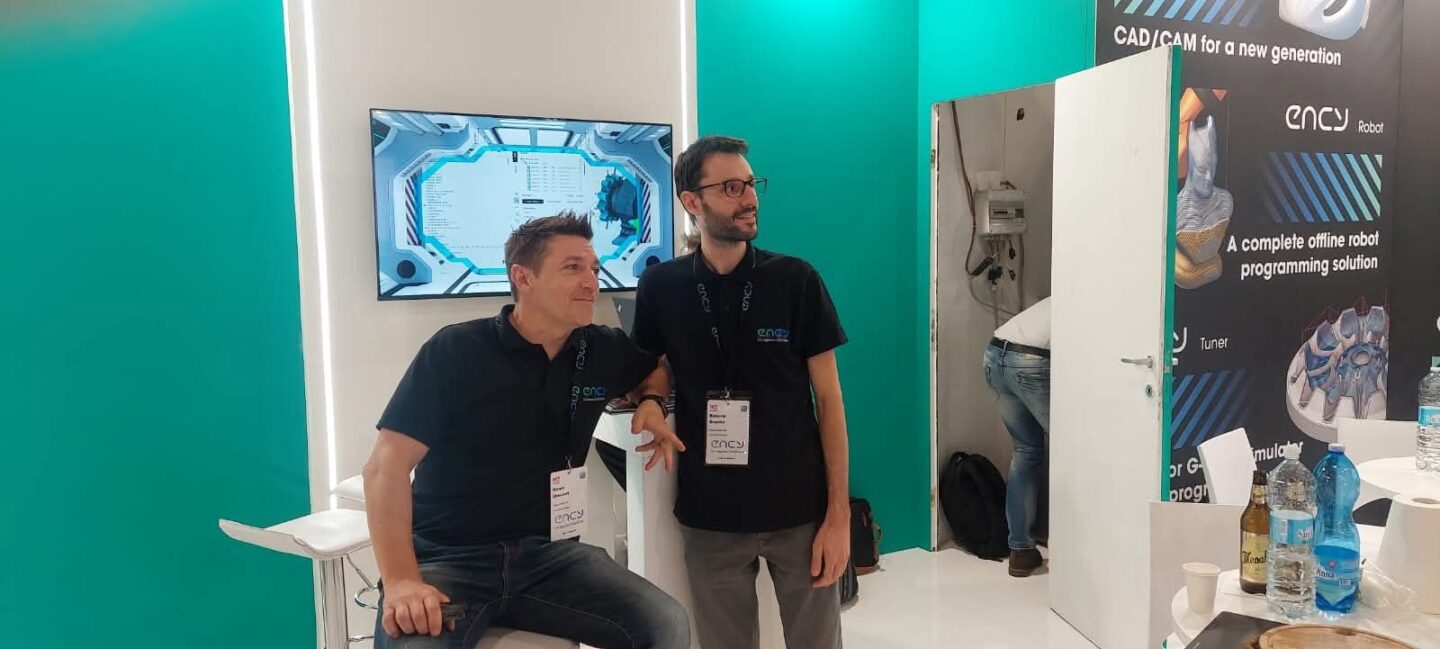 Two men stand together at a tech exhibition booth, engaged in discussion.