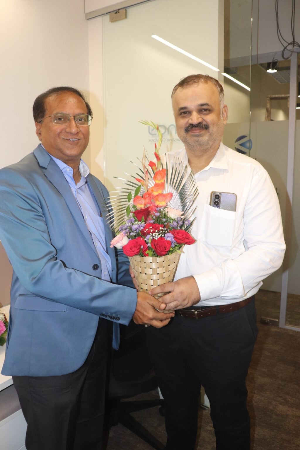 Two men exchange a flower bouquet in a warm, friendly gesture.