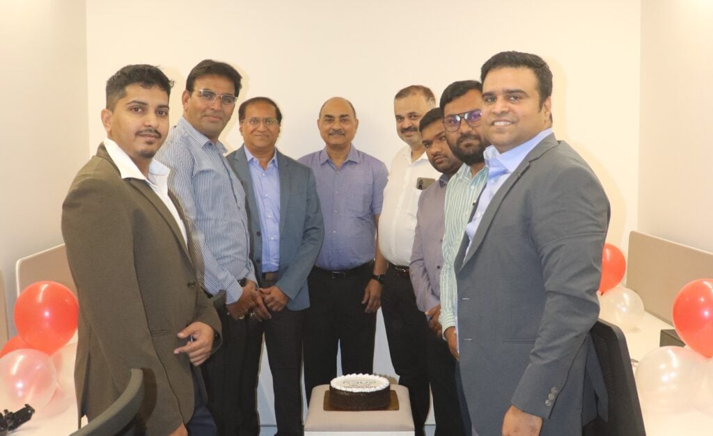 A group of eight men stands together, smiling around a cake.