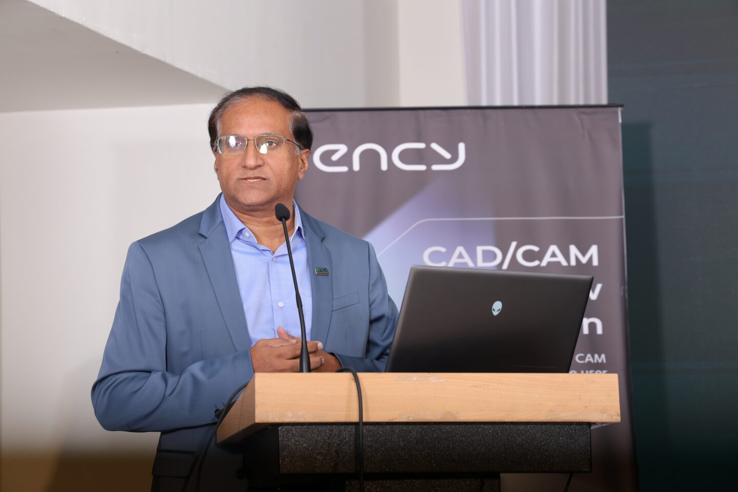 A speaker presents at a conference using a laptop and microphone.