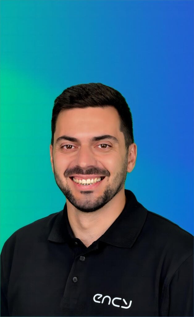 A smiling professional with short dark hair stands against a gradient background.