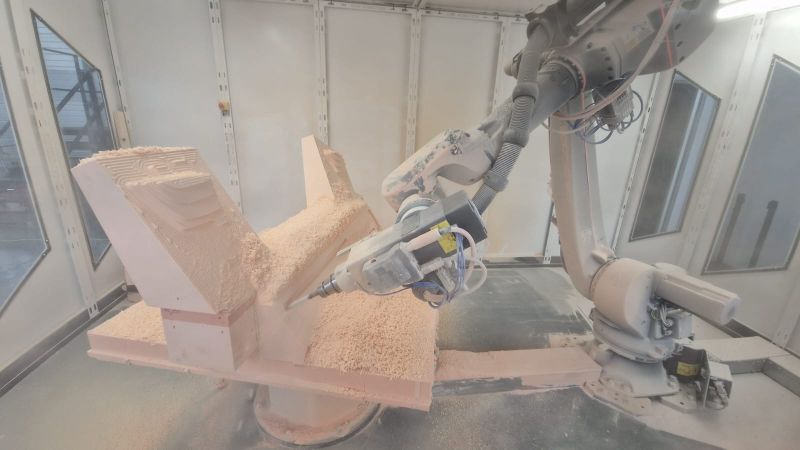 Bright orange industrial robot arm enclosed behind clear panels in a workstation labeled 'TRIM CELL'