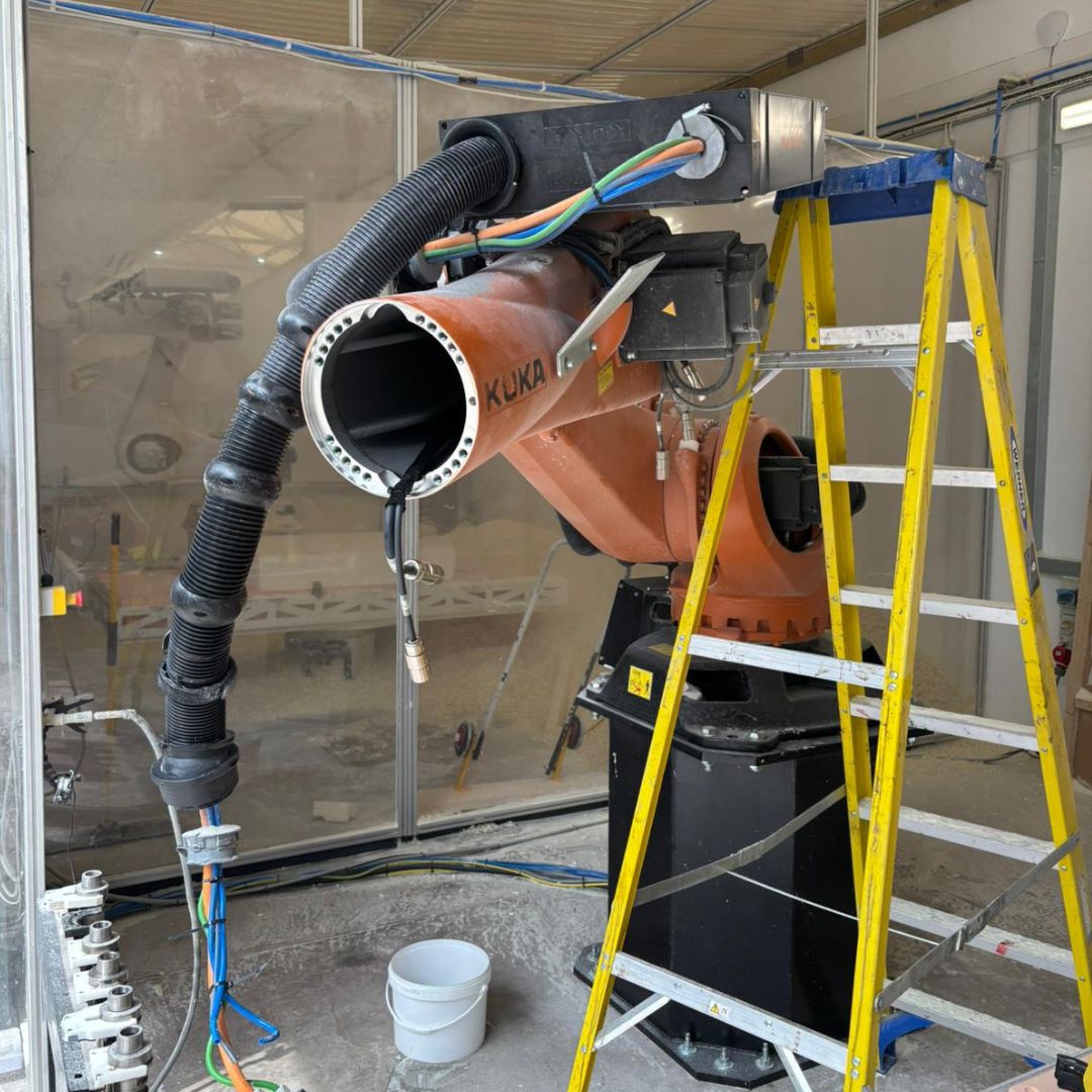 Bright orange industrial robot arm enclosed behind clear panels in a workstation labeled 'TRIM CELL'