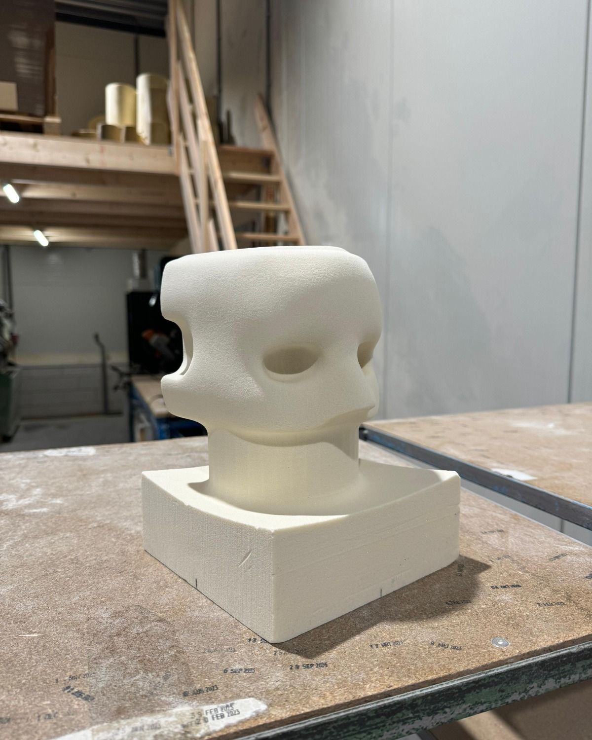 Six-axis industrial robot arm milling a light-colored foam or composite block into a contoured shape in an automated machining cell