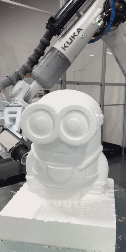 White six-axis industrial robot beside octagonal rotary table holding metal test coupons, with safety panels enclosing the cell