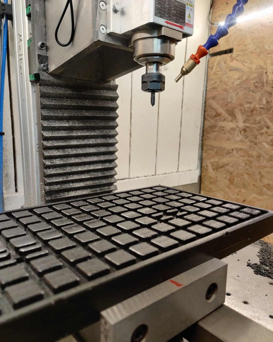Benchtop 3-axis CNC milling machine cutting square pockets into a workpiece with a small end mill and coolant hose