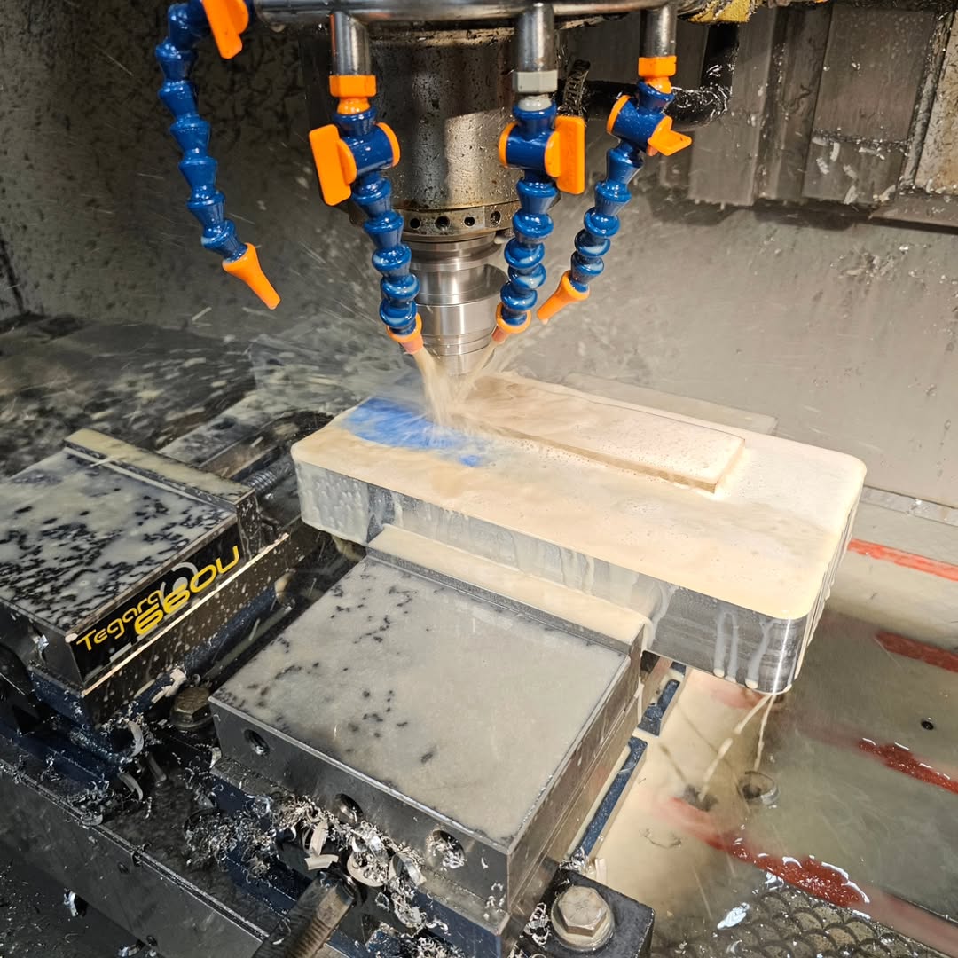 A white rectangular block clamped in a CNC milling machine's vise, with a rotating spindle milling a pocket into the top surface, coolant hoses visible, and the machine labeled 'Tegra S-80U'.