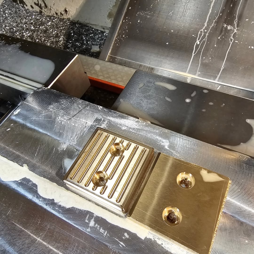 Metal workpiece inside CNC milling machine with coolant and chips, showing precision grooves and holes
