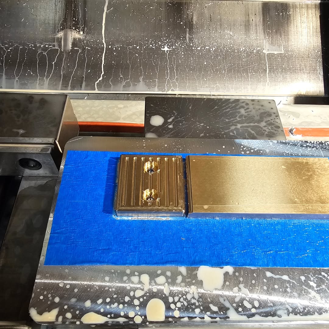 Rectangular metal workpiece clamped inside CNC milling machine with coolant residue