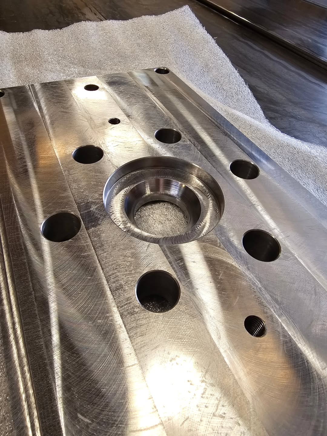 Metal fixture plate with central pocket and precisely machined holes, showing concentric milling marks