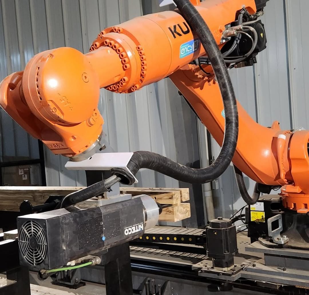 Orange KUKA six-axis industrial robot mounted on linear rails performing automated milling with a metal bracket