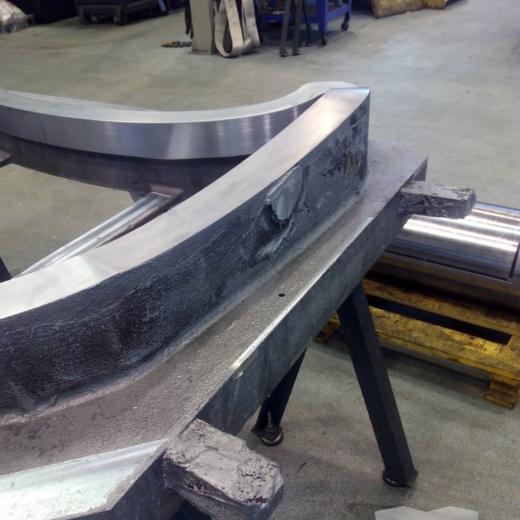 Large curved metal component with rough and finished surfaces resting on a shop-floor fixture during CNC milling