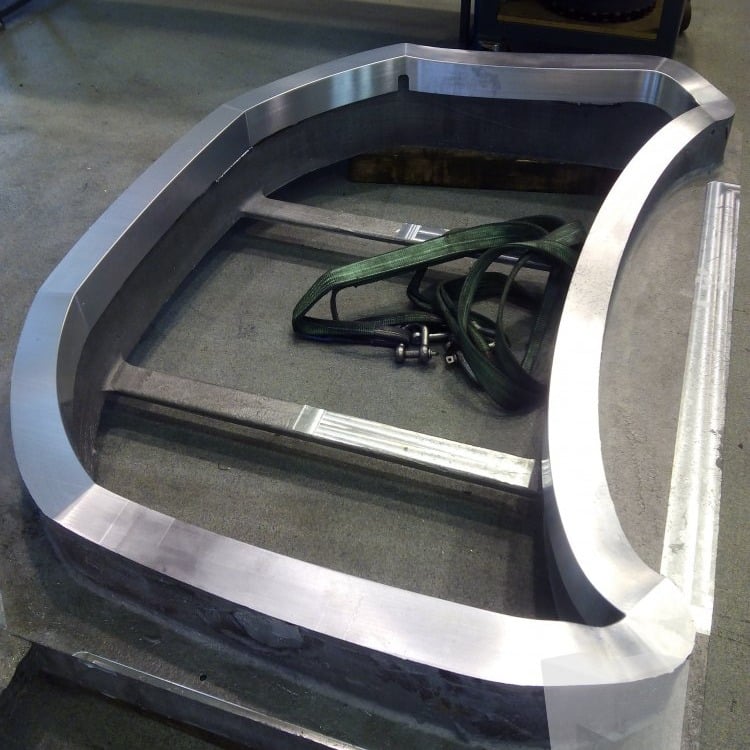 Large curved aluminum frame with smooth milled faces on a metal pallet in a machine shop