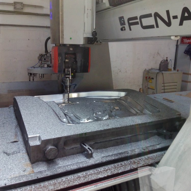 Large metal tooling blank being rough-machined on a gantry-style CNC milling machine with metal chips scattered around