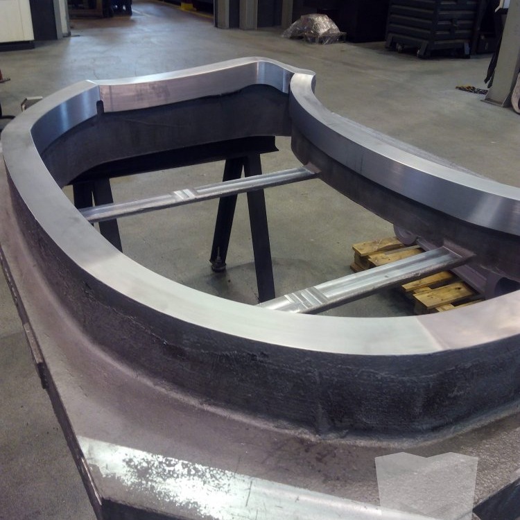 Large U-shaped metal casting with machined inner faces resting on support sawhorses in a workshop
