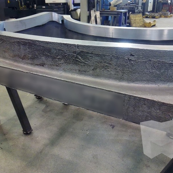 Large curved aluminum casting being machined on a CNC milling center with industrial robot in background