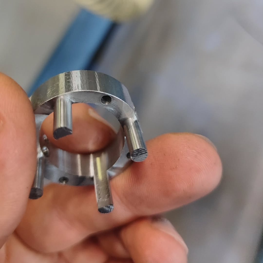 Close-up of a CNC-machined metal ring with four cylindrical pegs and cross-hatch marks