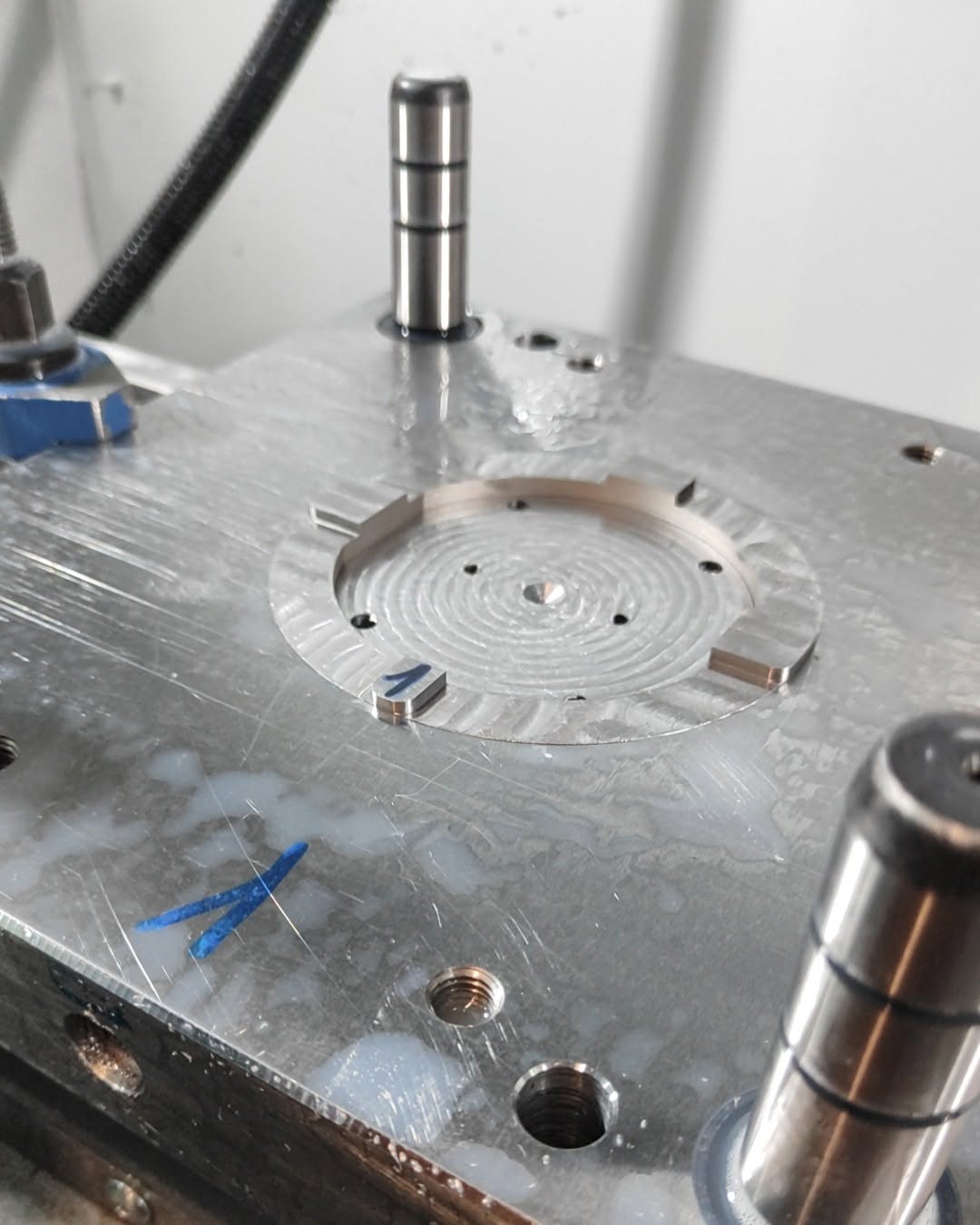 Circular metal plate with concentric machining marks secured between guide pillars on a CNC machine