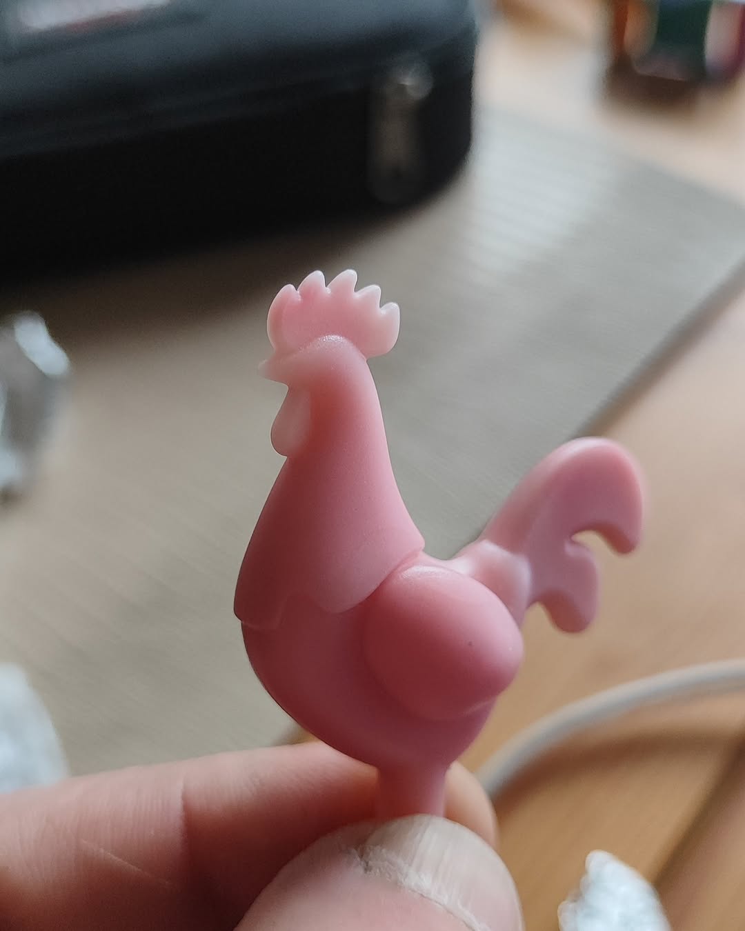 Small pink plastic rooster figurine held in hand against blurred tabletop background