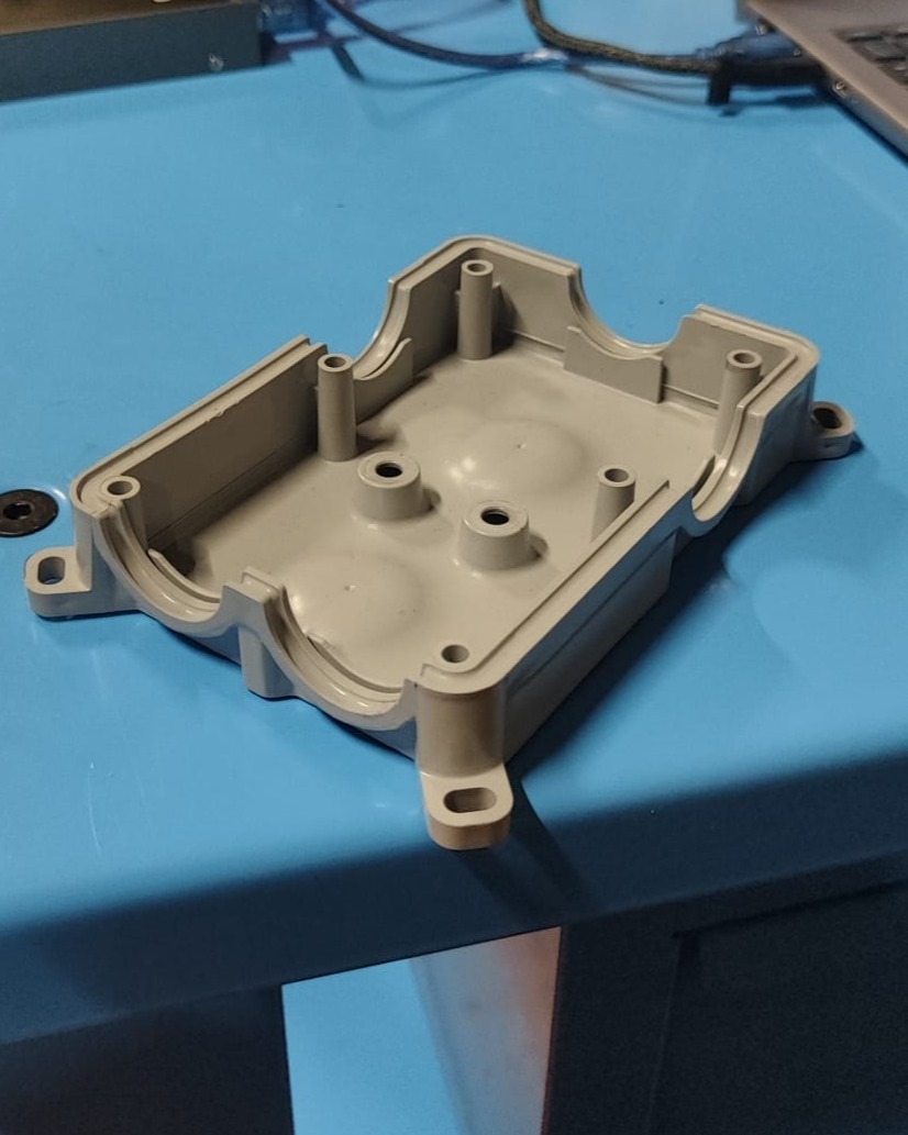 Beige injection-molded plastic housing sitting on a blue workbench with a laptop and cables in the background
