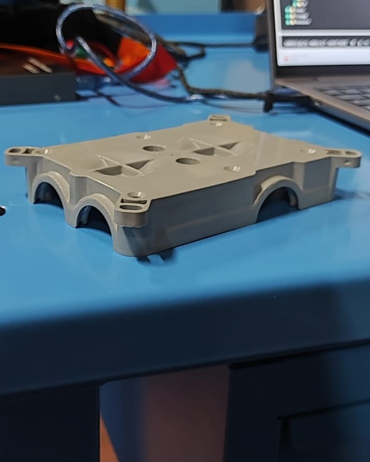 Gray plastic electronics housing with mounting flanges and precision holes on a blue workbench