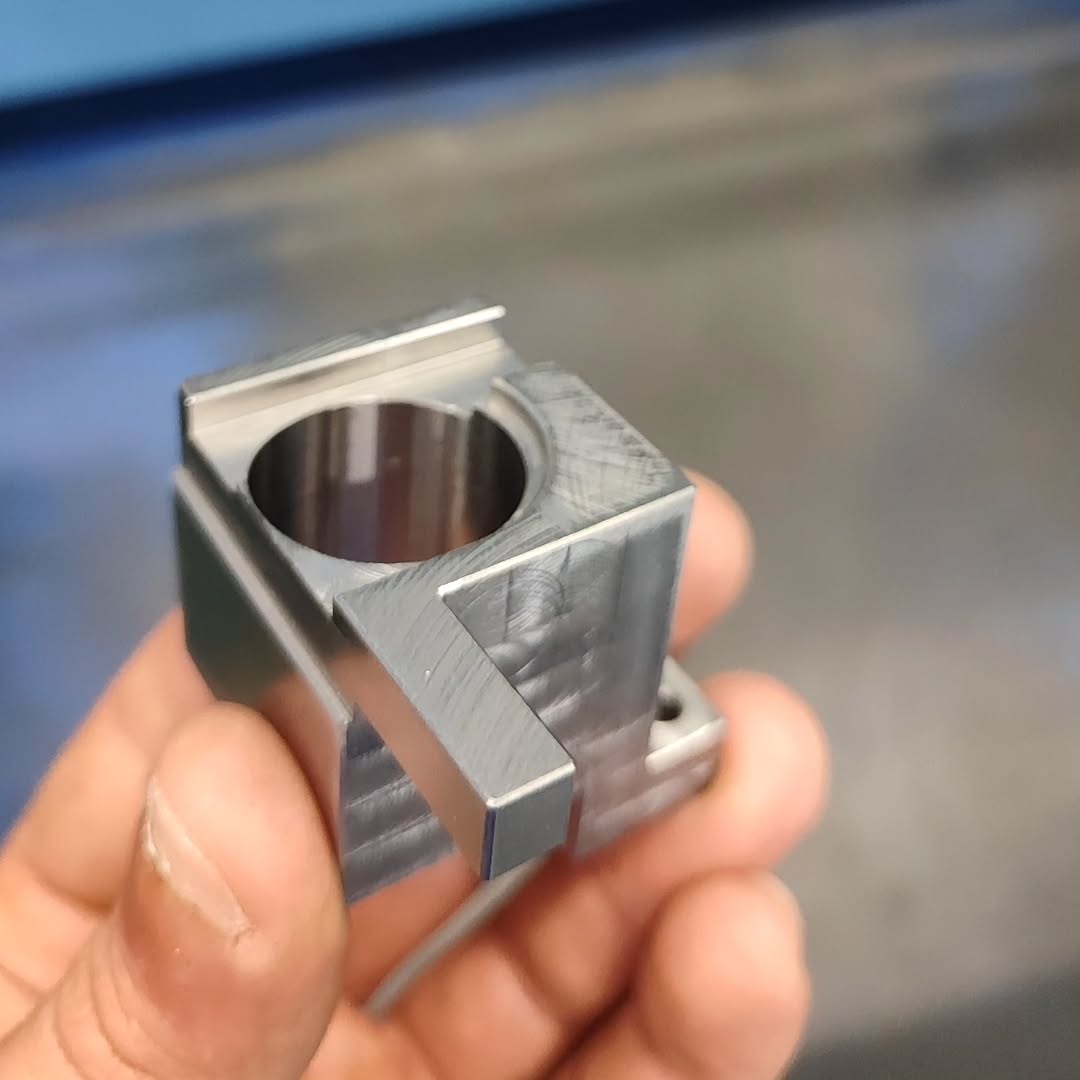 Close-up of a metal bracket with circular bore and multiple faces, showing CNC toolpaths