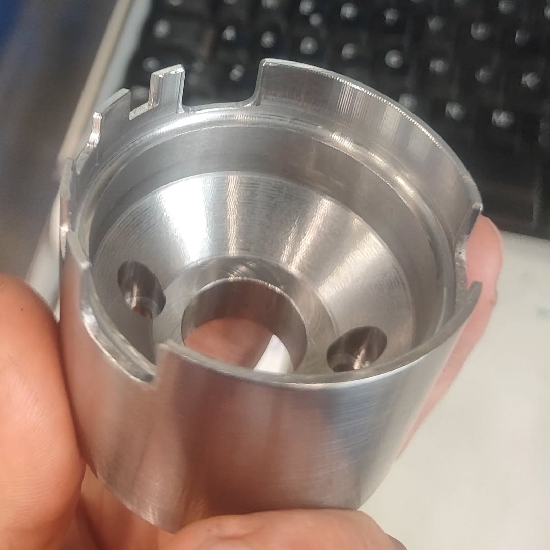 Close-up of a turned cylindrical metal workpiece with internal bores and external slots, held next to a computer keyboard