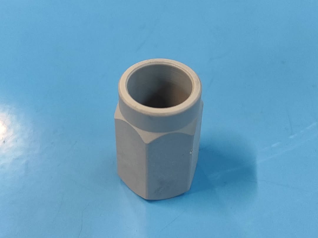 Gray hollow hexagonal prismatic component with smooth inner bore on light blue work surface