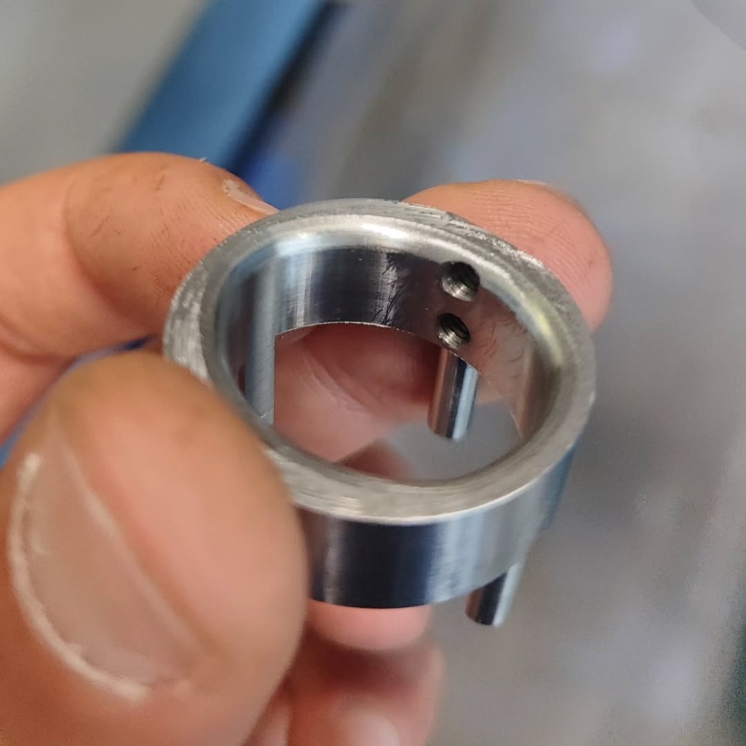 Close-up of a machinist's hand holding a small metal cylinder with drilled holes and internal cut-outs, produced on a CNC machine