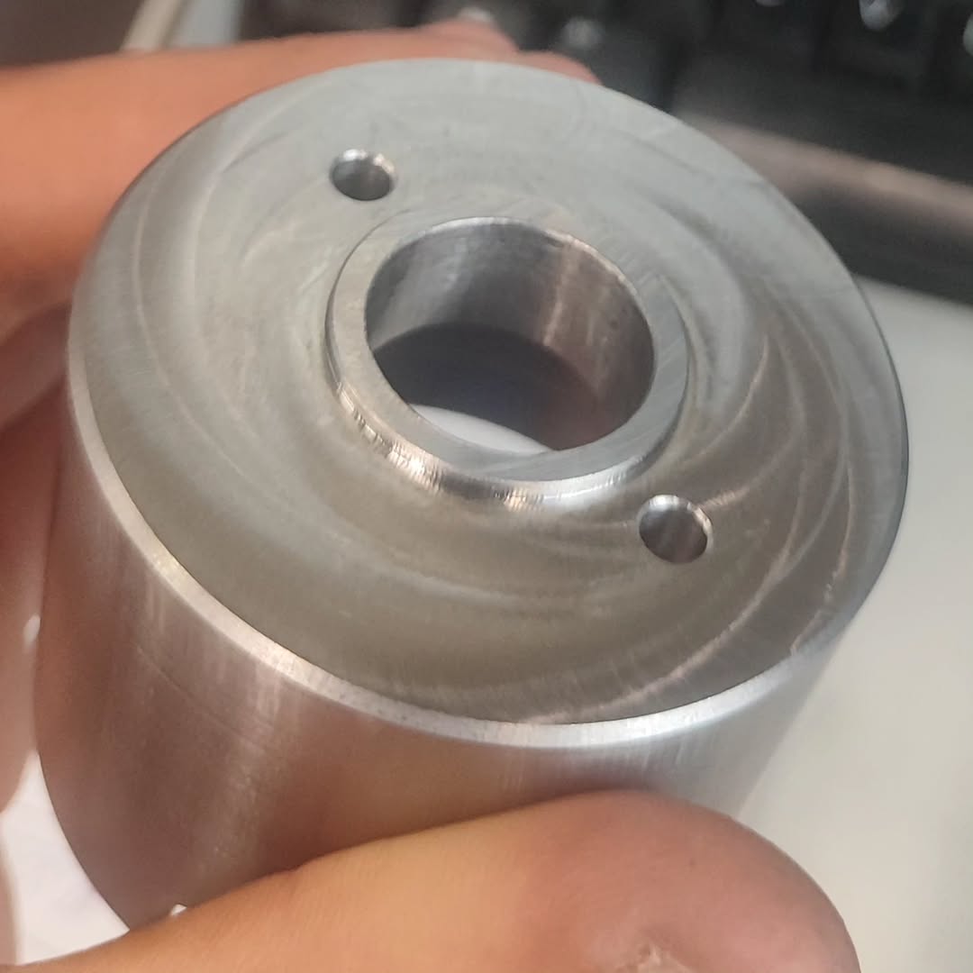 Hand-held cylindrical metal part with concentric machining marks and radial holes, produced by CNC turning